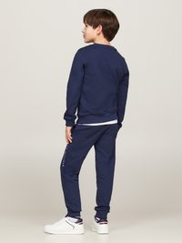 Marineblaue Sweatjacke mit gerippten Bündchen und Saum, kombiniert mit passenden Jogginghosen mit Logodetails am Oberschenkel, getragen mit weißen Sneakers.