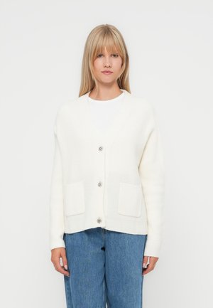 Witte gebreide cardigan met een V-hals, twee voorzakken en zilveren knopen. Zachte textuur en een ontspannen pasvorm. Draag je over een witte top.
