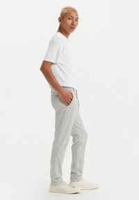 Light gray straight-leg pants feature front pockets and a subtle logo, paired with a plain white t-shirt and white sneakers.