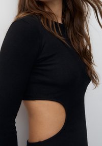 Robe noire côtelée avec des manches longues, une silhouette ajustée et un détail découpé distinctif à la taille pour un intérêt visuel supplémentaire.