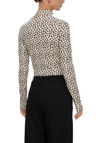 Długi rękaw w jasnym beżowym kolorze z wzorem w panterkę w czerni i czerwieni. Wysoki kołnierz, dopasowany krój, wykonany z miękkiego, elastycznego materiału.