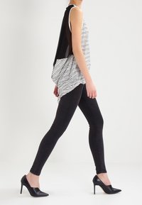 Top senza maniche a righe con un pannello nero, abbinato a jeans skinny neri e tacchi alti neri. Texture liscia, vestibilità rilassata.