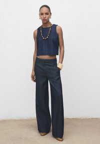 Donkerdenim crop top en wijde broek, met een gladde textuur en strakke lijnen. Accessoires zijn onder andere een houten kralenketting en armbanden.