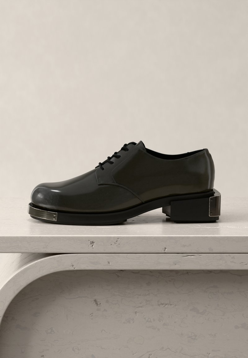 Black leather oxford shoe with square metal accents on toe and block heel, displayed on a light marble surface against a plain background.