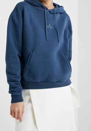 Felpa blu con cappuccio realizzata in tessuto morbido, caratterizzata da una tasca frontale, polsini a costine e un piccolo logo a forma di gruccia sul petto.