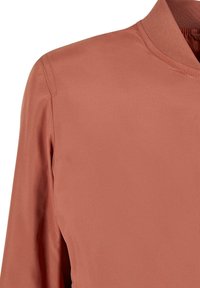 Veste bomber en satin couleur rouille avec col côtelé et couture visible à l'épaule sur fond uni.