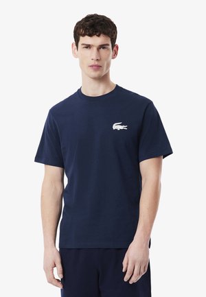 T-shirt en coton bleu marine à manches courtes et col rond, avec un logo de crocodile blanc sur la poitrine gauche.