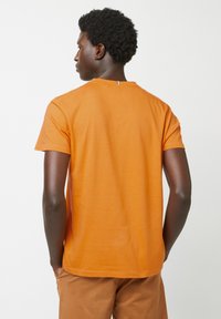 Oranje T-shirt met korte mouwen van zachte stof, voorzien van een ronde halslijn en een klein accent aan de achterkant van de hals. Eenvoudig ontwerp, casual fit.