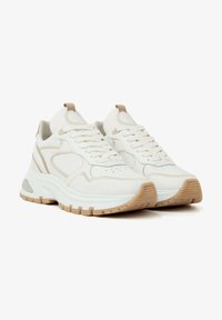 White athletic sneakers with a textured upper, beige accents, a thick sole, and a lace-up design featuring perforations for breathability.