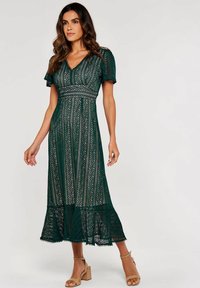 Grünes Maxikleid aus Spitze mit kurzen Puffärmel, V-Ausschnitt, aufwendigen Mustern und einem ausgestellten Saum. Verfügt über einen strukturierten Stoff mit dekorativen Akzenten.