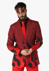 Traje rojo con patrones de llamas negras, incluyendo una corbata a juego. Textura de satén, corte clásico con cierre de un solo botón y camisa negra debajo.