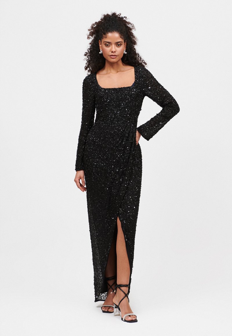 Abito nero in paillettes con maniche lunghe, scollo quadrato e uno spacco laterale. Tessuto morbido e strutturato con una silhouette aderente.