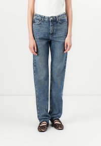 Jeans din denim albastru cu talie înaltă și croială dreaptă, cu buzunare laterale și textură subtilă. Asortate cu pantofi tip balerin cu imprimeu animal.