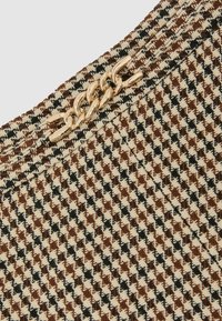 Rudos ir kreminės spalvos audinio raštas su šunų danties motyvu, paauksuoto grandinėlės akcentas ir užtrauktuko uždarymas viršutinėje kraštinėje. Tekstūra atrodo austinė.