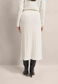 White ribbed midi skirt with a fitted waistband, paired with glossy black knee-high boots. The fabric has a soft, textured appearance.