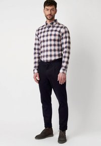 Overhemd met knopen in een ruitpatroon, met tinten blauw, crème en bordeauxrood. Gepaard met donkere broek en bruine suède schoenen.