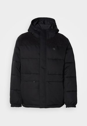 Casaco preto acolchoado com capuz, apresentando um fecho de correr, punhos elásticos e detalhes em camurça nos ombros para adicionar textura.