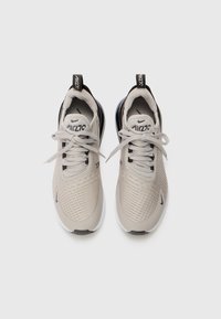 Paire de baskets Nike Air270 beige avec lacets noués, languettes noires et semelles blanches sur un fond clair uni.