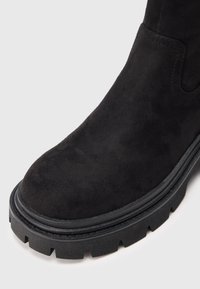 Must mustelaste ankle boot, millel on ümar varvas ja paks must kummist tall, millel on tekstuuriga disain ja peened õmbluse üksikasjad.