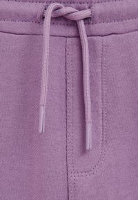 Lilac kokvilnas sporta bikses ar elastīgu jostu, kurai ir noapaļoti plastmasas gali un sānu kabata. Redzama mašīnas adīta tekstūra.
