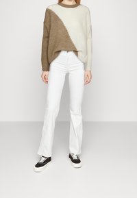 Ruskean ja kermaisen värin päivätyö neule takki viisto kuvio, yhdistetty valkoisiin leveälahkeisiin farkkuihin ja mustiin tennareihin, joissa on valkoiset nauhat.