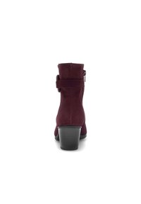 Botas de tobillo de ante burdeos con tacón apilado, cremallera lateral y una correa decorativa alrededor del tobillo. Textura suave y diseño ajustado.