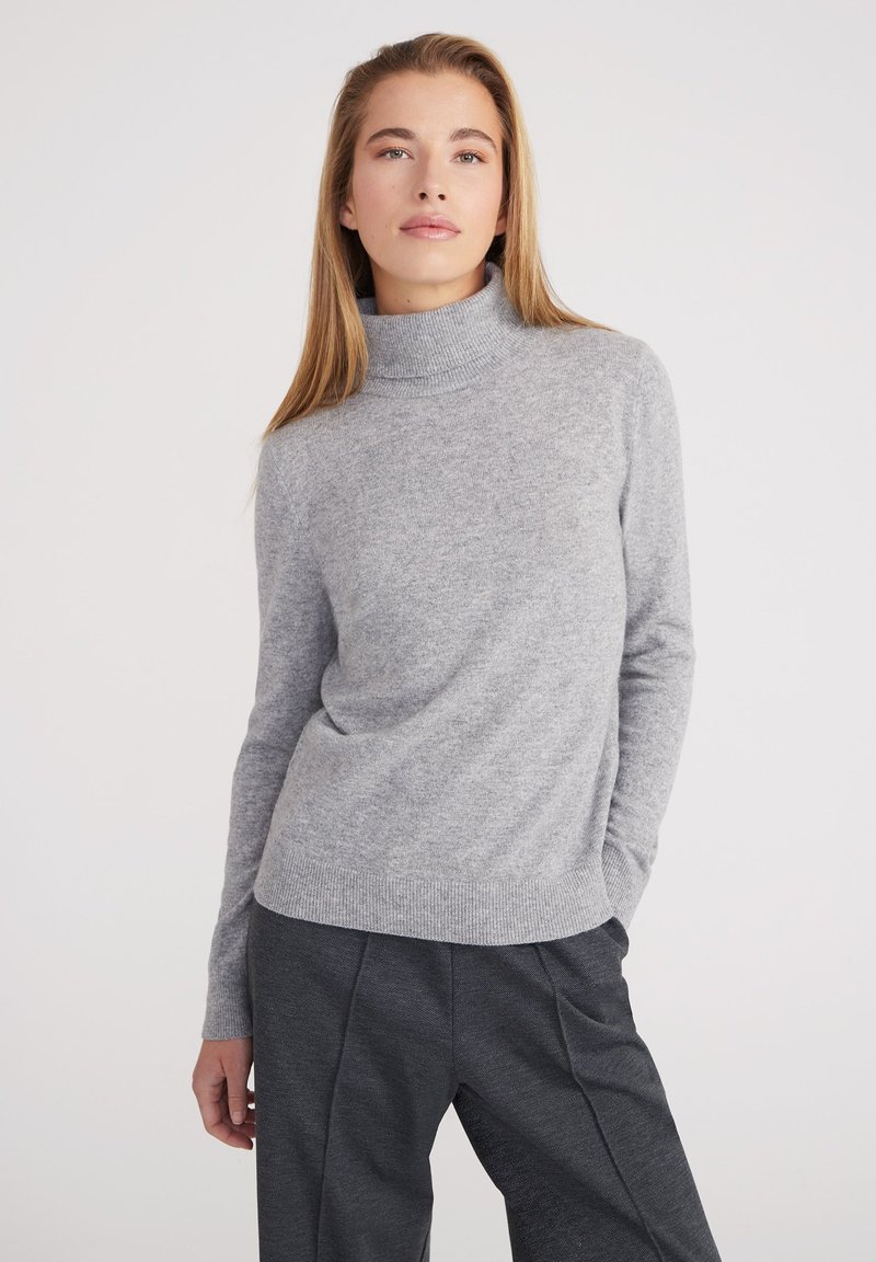Maglione grigio chiaro a collo alto in un morbido tricot, con maniche lunghe e vestibilità rilassata. L'orlo e i polsini a coste aggiungono una leggera texture.