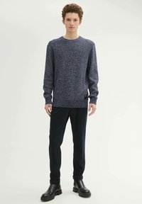 Granatowy sweter dzianinowy z teksturowanym wzorem, z okrągłym dekoltem i długimi rękawami. W połączeniu z ciemnymi spodniami i czarnymi botkami za kostkę.