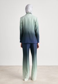 Maßgeschneiderter Anzug in einem Farbverlauf von Grün zu Marineblau, aus einem Stoff mit glatter Textur; umfasst einen passenden Hijab. Die Rückansicht zeigt ein schlichtes Design.