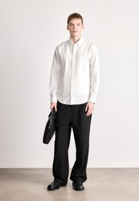 Λευκό πουκάμισο με γιακά, μαύρο παντελόνι με φαρδιά πόδια και μαύρη δερμάτινη τσάντα. Λείο ύφασμα και καλοσχηματιστή εφαρμογή.