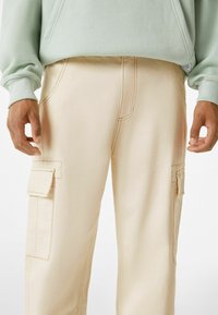 Beige cargo kalhoty s hladkou strukturou, výrazným šitím a detaily bočních kapes, stylizované s mentolově zelenou mikinou.