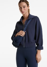Marineblaue, taillierte Zip-Jacke aus strukturiertem Stoff, mit einem breiten Kragen und umgeschlagenen Ärmeln, kombiniert mit passenden, hoch taillierten Leggings.