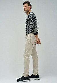 Camisa de manga larga a rayas en blanco y negro, pantalones beiges y zapatillas negras. La camisa tiene un cuello redondo y un diseño ajustado. Los pantalones cuentan con bolsillos.