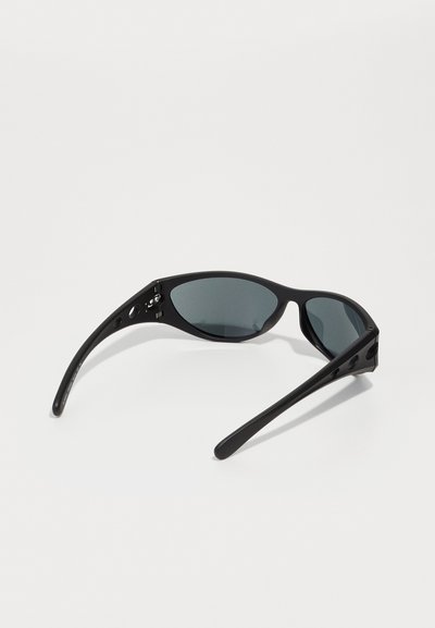 Lunettes de soleil noires avec un design élégant, dotées de verres teintés, d'une forme courbée et de branches allongées avec des accents découpés.