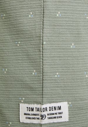 Jasnozielona tkanina o fakturze z małymi wielokolorowymi wzorami w kropki i białą prostokątną metką z napisem Tom Tailor Denim.