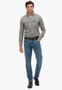 Graues Hemd mit Kragen und zwei Brusttaschen, kombiniert mit blauen Jeans und schwarzen Stiefeletten. Glatter Stoff und taillierte Passform.