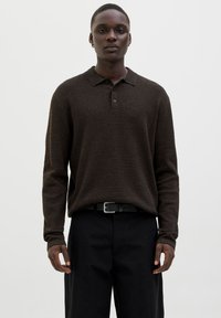 Brauner gestrickter Polopullover mit langen Ärmeln, Knopfleiste mit fünf Knöpfen und strukturiertem Stoff, kombiniert mit schwarzen hochgeschnittenen Hosen und einem Gürtel.