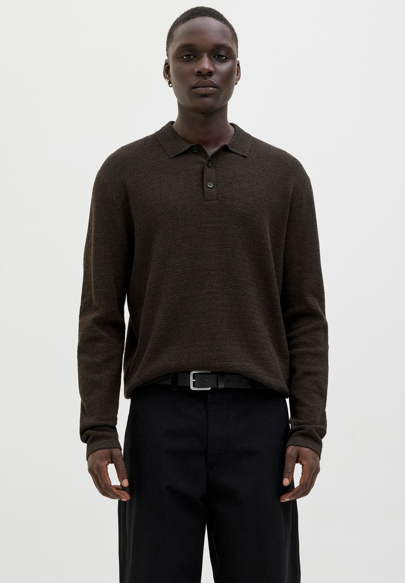 Brauner gestrickter Polopullover mit langen Ärmeln, Knopfleiste mit fünf Knöpfen und strukturiertem Stoff, kombiniert mit schwarzen hochgeschnittenen Hosen und einem Gürtel.