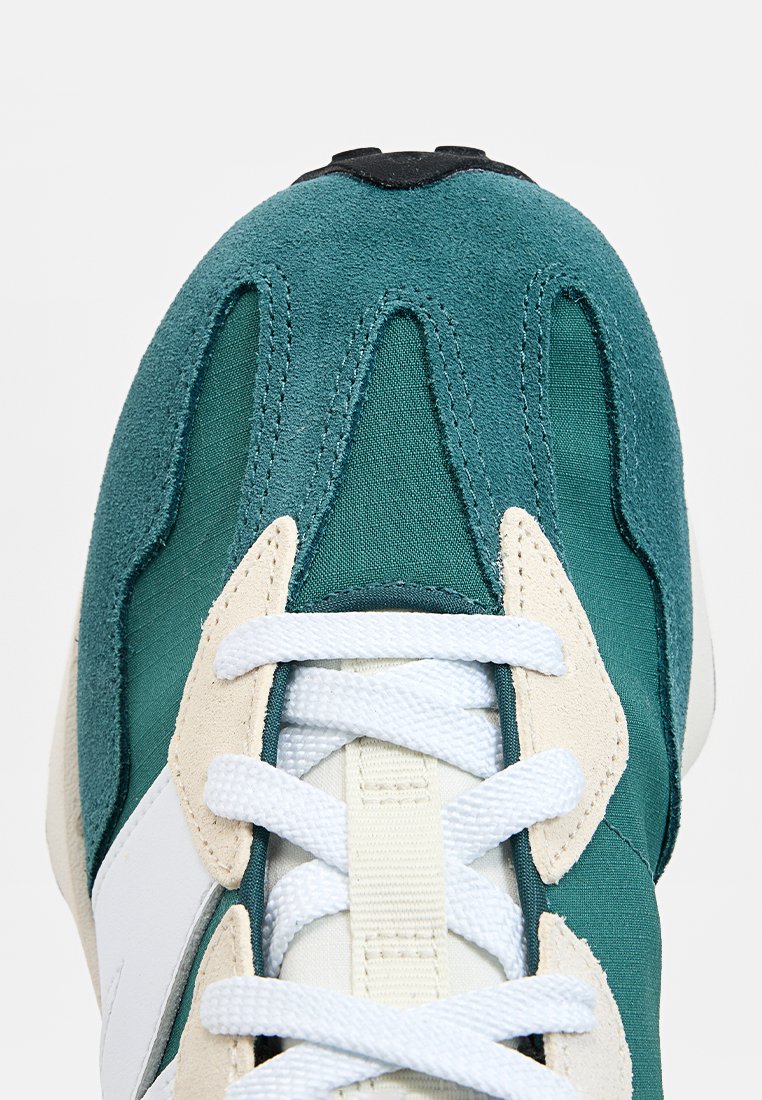 Baskets en suède vert et mesh avec des lacets blancs, des accents beige et une tige texturée ornée de coutures en zigzag distinctes.