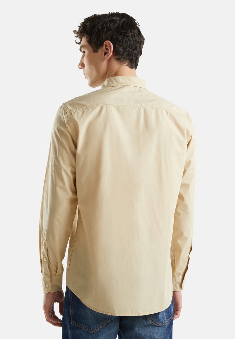 Lichtbeige langemouwen shirt met een puntige kraag, knoopmanchetten en een gebogen zoom; gemaakt van zachte katoen stof.