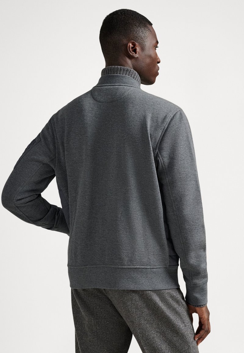 Polaire grise avec col montant, col côtelé et panneaux latéraux. Texture lisse et coupe décontractée. Portée avec un bas gris assorti.