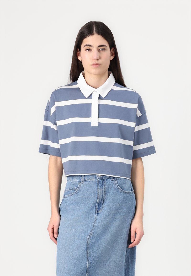 T-shirt polo cortado em azul com riscas horizontais brancas, apresentando um colarinho branco e mangas curtas. Combinado com uma saia de ganga azul clara.