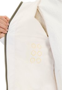 Weißer Fleece-Jacke mit einem seidigen Innenfutter in Netzstruktur. Innen sind gelbe Kreise auf einem cremigen Hintergrund bedruckt. Mit Reißverschluss.