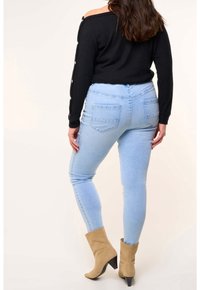 Pull noir à côtes décontracté avec des accents de boutons, associé à un jean skinny bleu clair et des bottines à talons beiges.