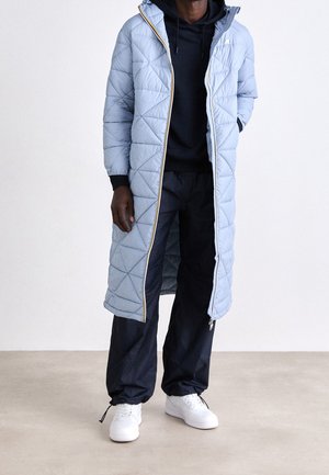 Vaaleansininen tikattu pitkä takki hupulla ja kultaisella vetoketjulla, yhdistetty mustaan huppariin, tummiin housuihin ja valkoisiin lenkkareihin.