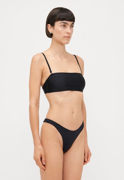 Melnā bikini komplektā ietilpst bezplecu bandeau tops un augsti griezti apakšdaļa. Gluda auduma ar minimālistisku dizainu un regulējamām siksnām.