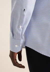 Blauw-witte gestreepte lange mouwen shirt met een knoopmanchet en een zwart geborduurde roosdetail op de mouw.