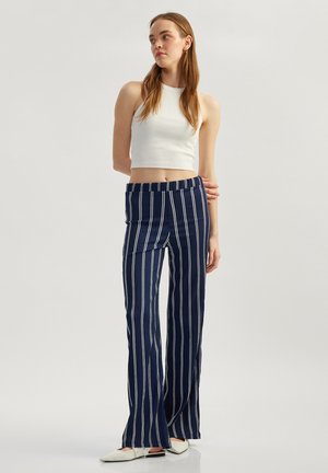 Marineblå og hvide stribede bredbåndede bukser med elastisk talje; parret med en tætsiddende hvid crop top og hvide spidse sko. Glat tekstur.