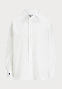 Valkoinen pitkähihainen nappipaita, jossa on terävä kaulus ja pieni tumma brodeeraus vasemmassa hihassa.