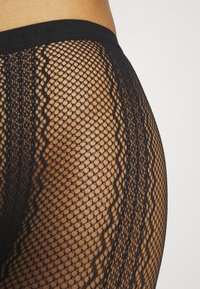 Collants en résille noire avec un motif ondulé, dotés d'une taille élastique douce et d'un design à mailles ouvertes pour une meilleure respirabilité.